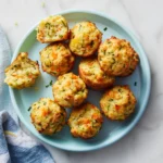 Golden bite-sized veggie muffins with carrots, zucchini, and cheese served on a kid-friendly plate over a white marble table.