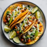 Roasted sweet potato and black bean tacos with avocado and lime crema on a colorful plate over a white marble table.